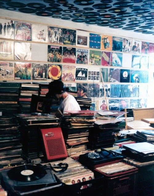 Cluttered Asian record shop with stacks of vinyl on tables and covers pinned to the ceiling